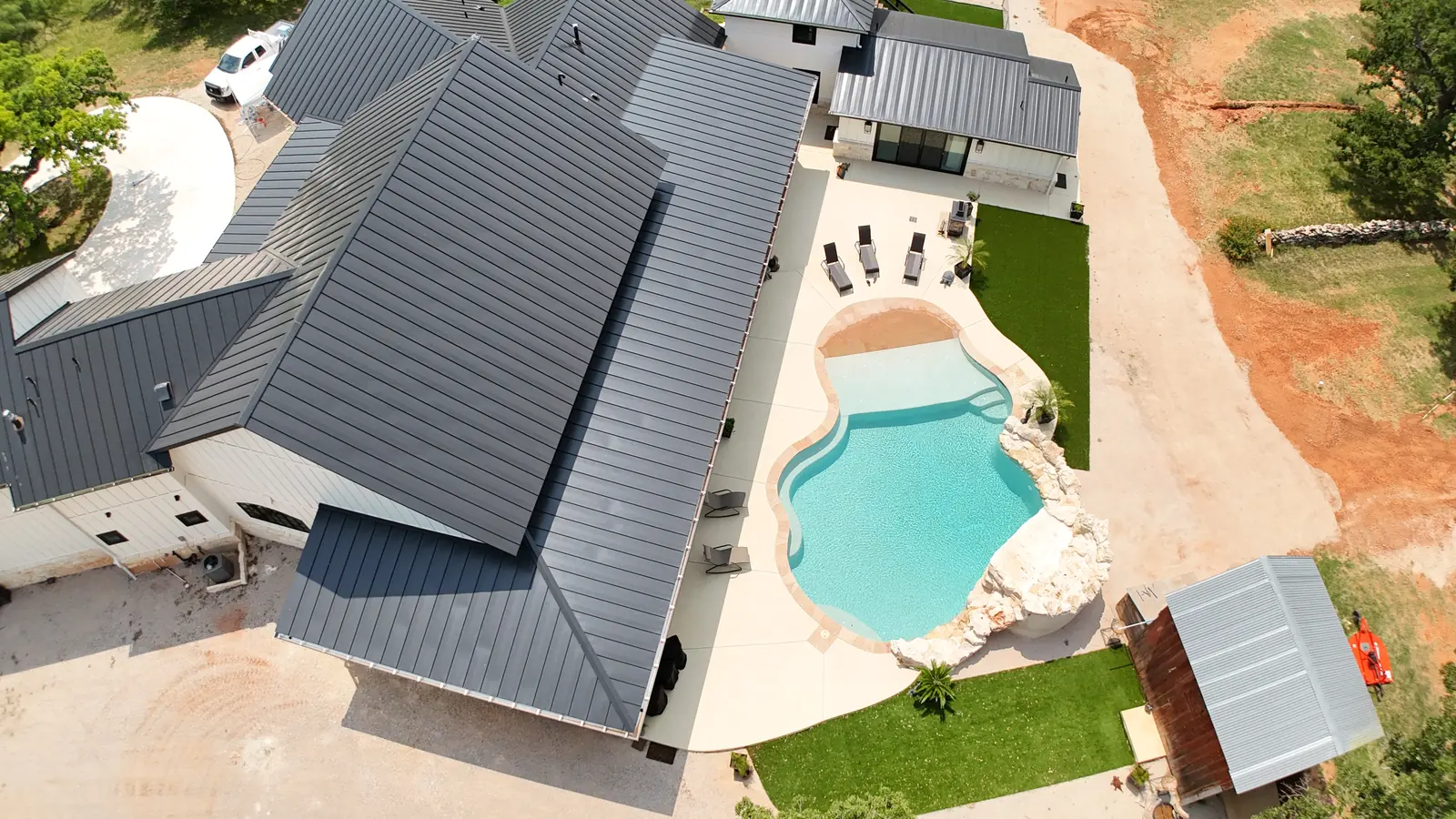 Aerial view of a custom home with dark metal roof, backyard pool and turf lawn