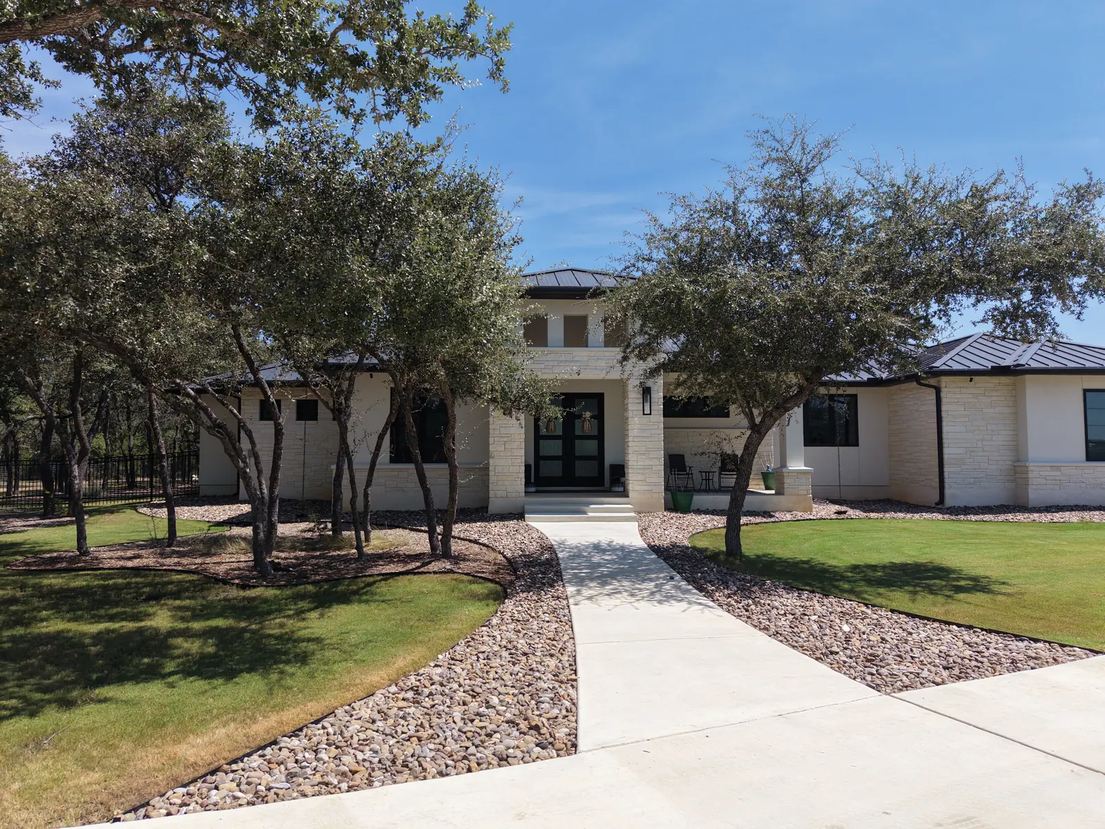 Completed white stone custom home with dark metal roof and landscaped yard, seen from above