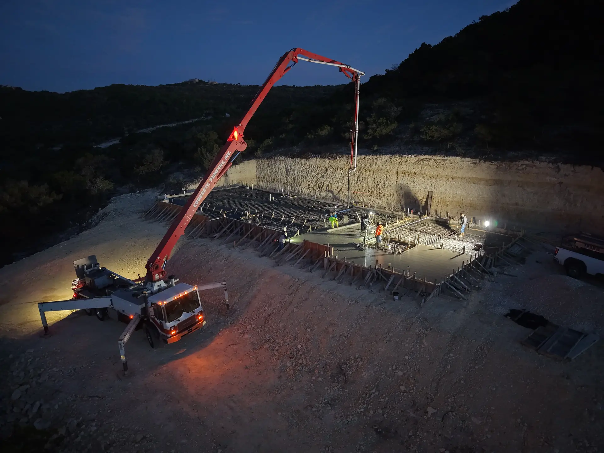 Concrete boom pump pouring a foundation under work lights before dawn