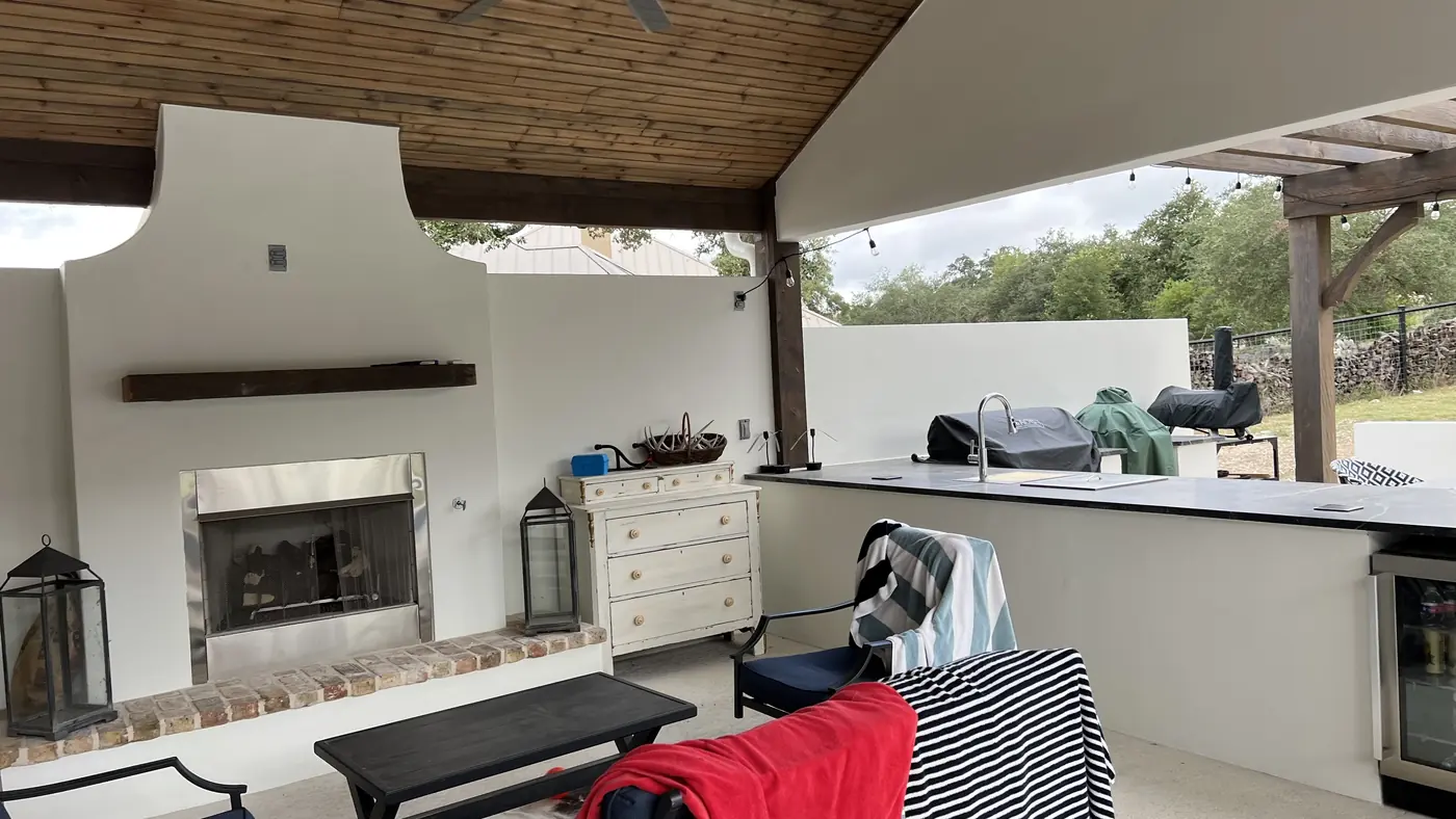 Outdoor kitchen with fireplace under a wood-ceiling covered patio